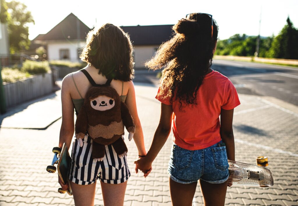 Rear view of teenager girls friends with skateboards outdoors in city